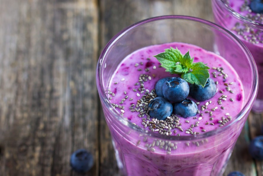 A glass of smoothie topped with blueberries and chia seeds.